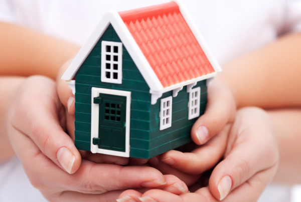 Two sets of hands holding a green house for home planning