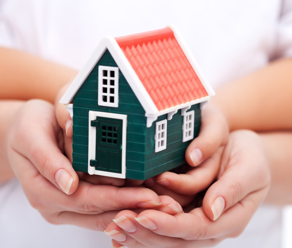 Two sets of hands holding a green house for home planning