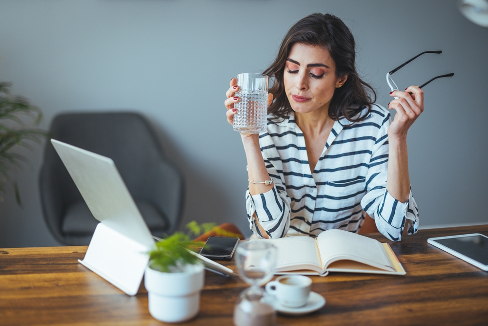 A woman sipping her water and reading her planner to discuss a mid-year financial reset