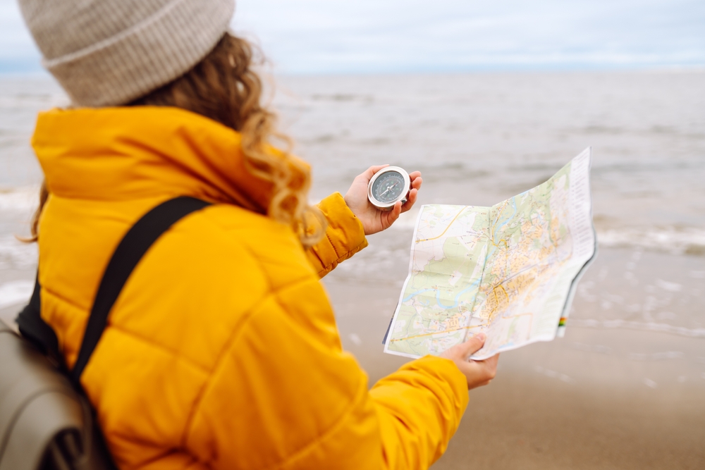 a woman looking at a compass and map on the beach in reference to market volatility